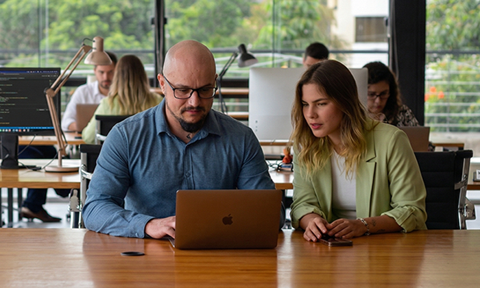 Um homem e uma mulher sentados a mesa, olhando resultados em seu notebook